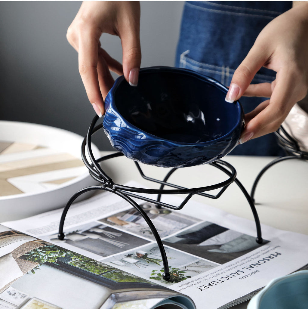 Blue ceramic pet bowl being placed in its elevated metal stand