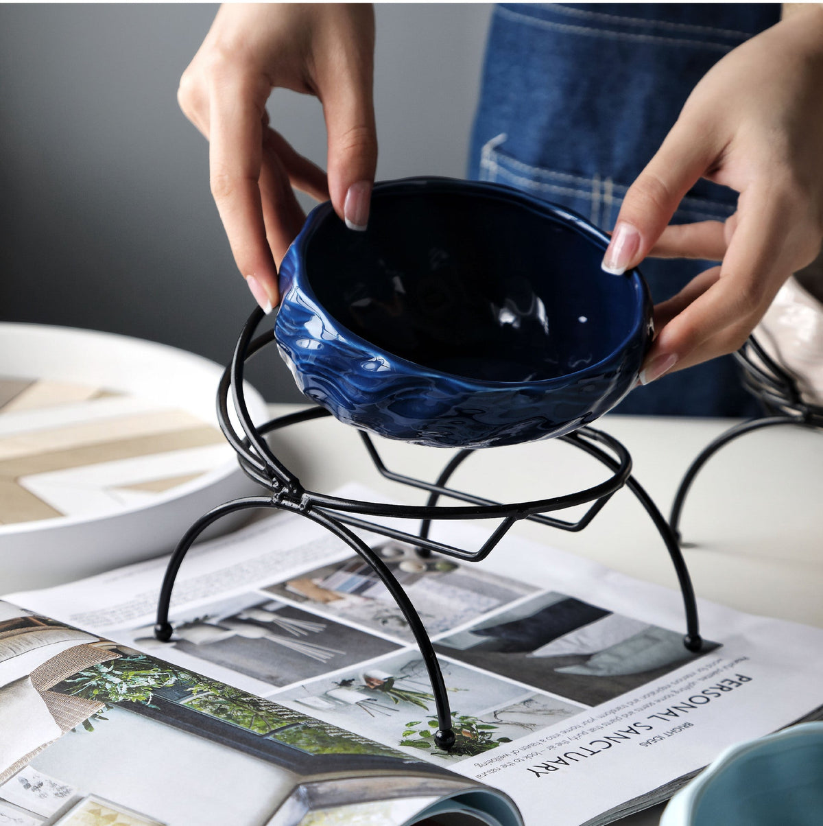 Blue ceramic pet bowl being placed in its elevated metal stand