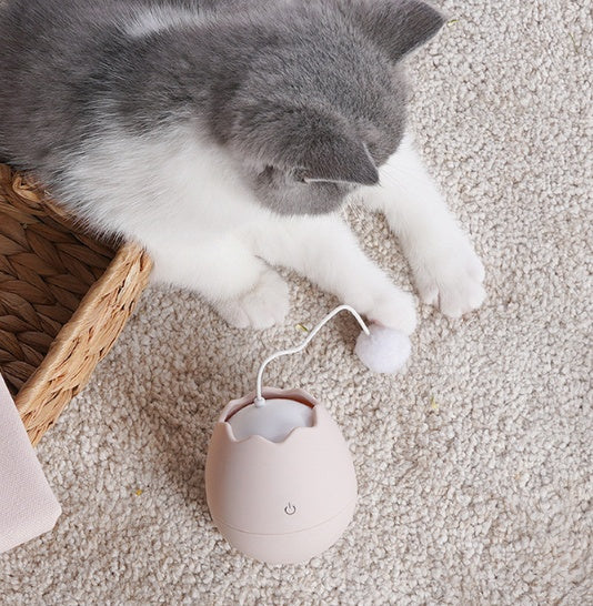 Cat reaching for the pink interactive toy's pom-pom